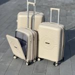 Чемодан Mybag Krug молочный, вид под углом три четверти сверху с поднятой выдвижной ручкой, открытым дополнительным отделением рядом с чемоданами молочного цвета с поднятыми ручками